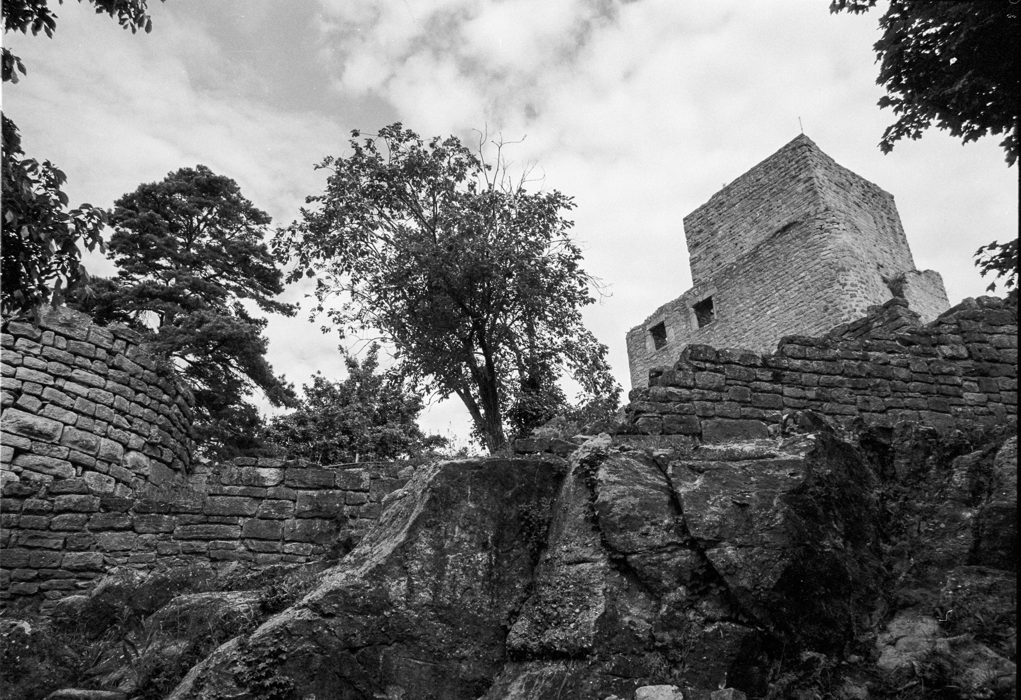 Tour d’une forteresse en ruine dominant un mur de pierre et un affleurement rocheux en noir et blanc