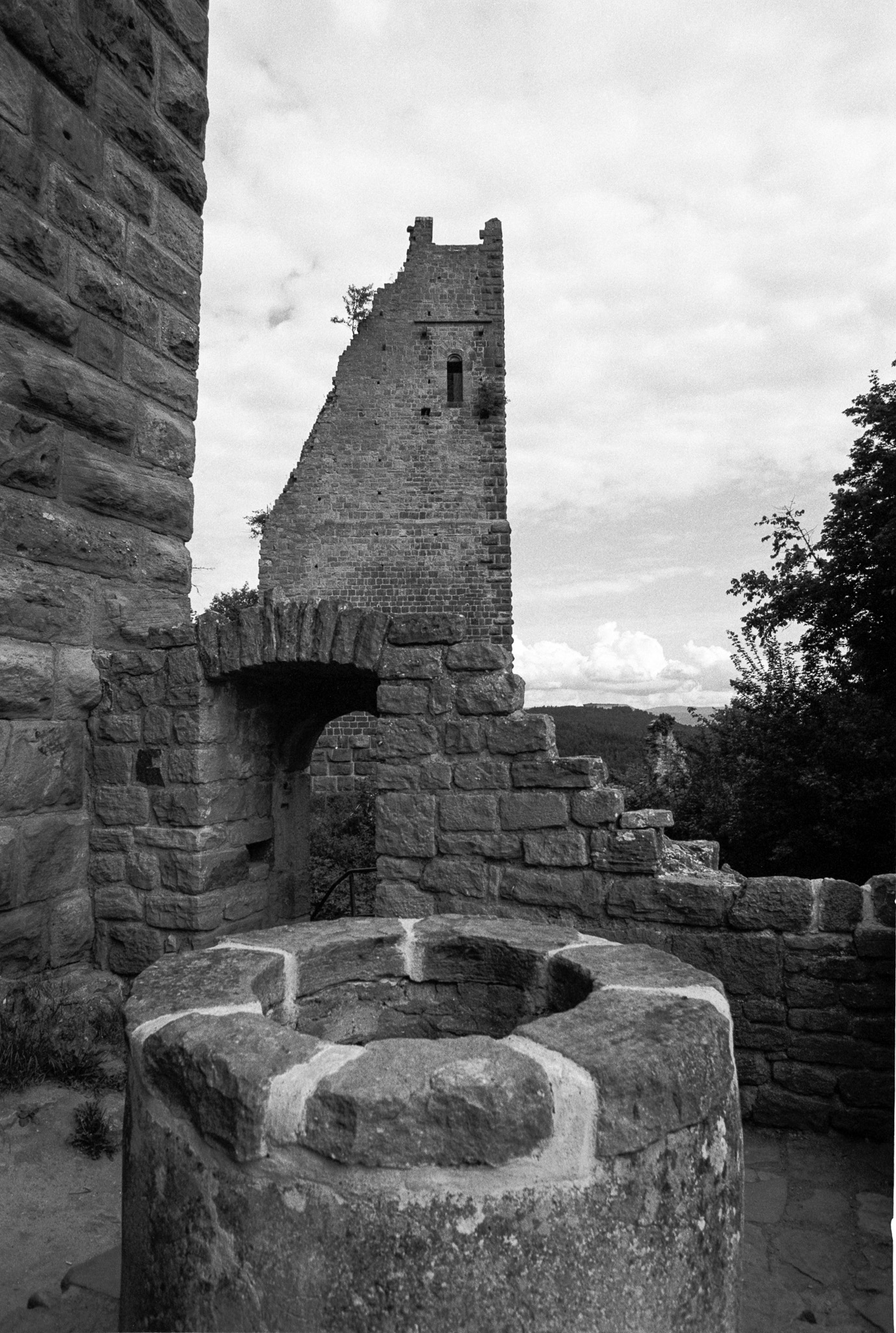 Ancien puits de pierre au premier plan devant les vestiges d’une forteresse en noir et blanc