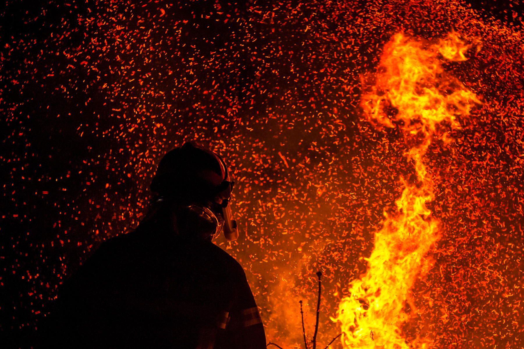 Silhouette de sapeur-pompier devant un feu et des gerbes d’étincelles lors d’un exercice de nuit