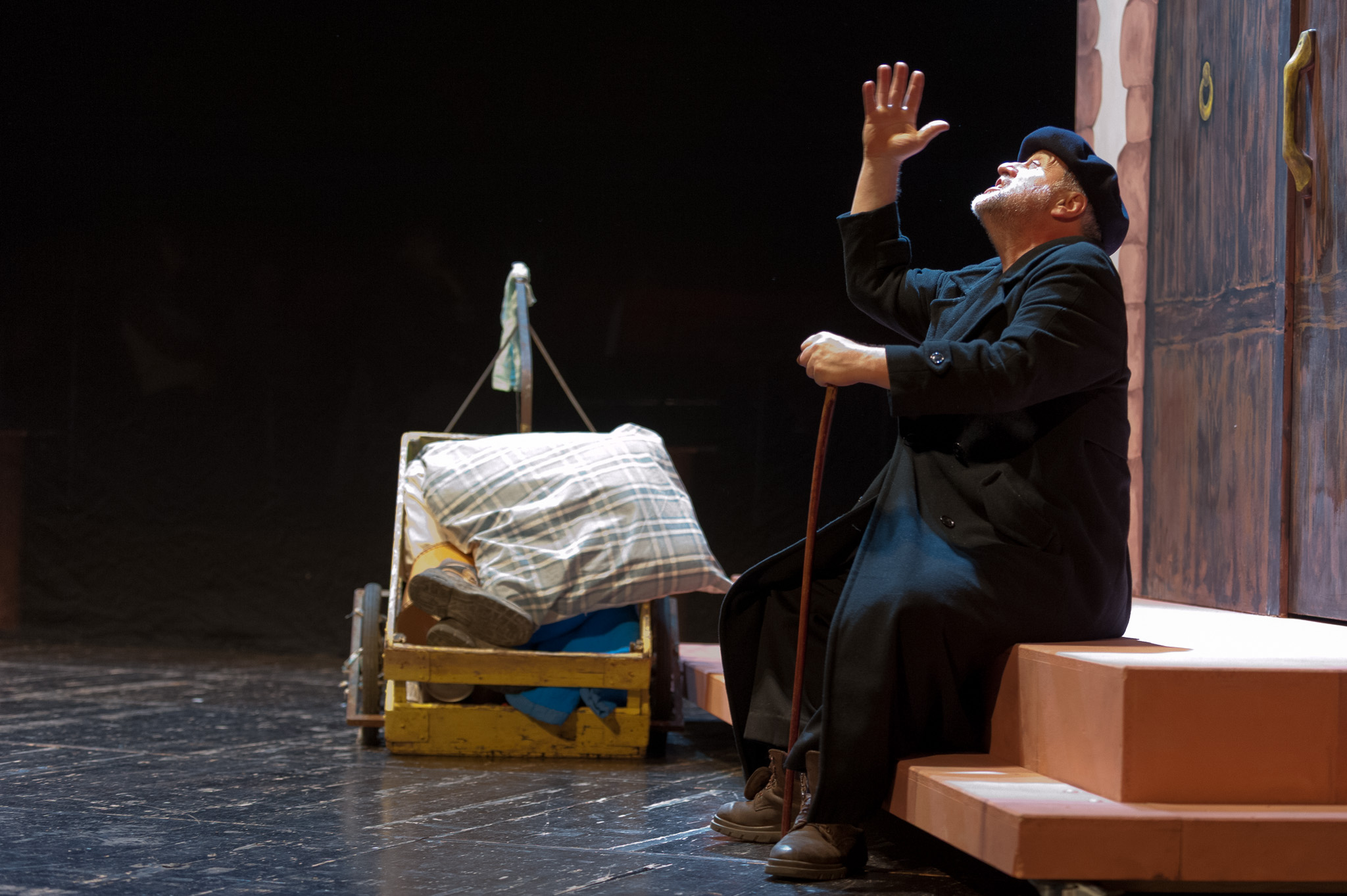 Comédien seul sur une scène de théâtre alsacien, la main levée près d’un élément de décor