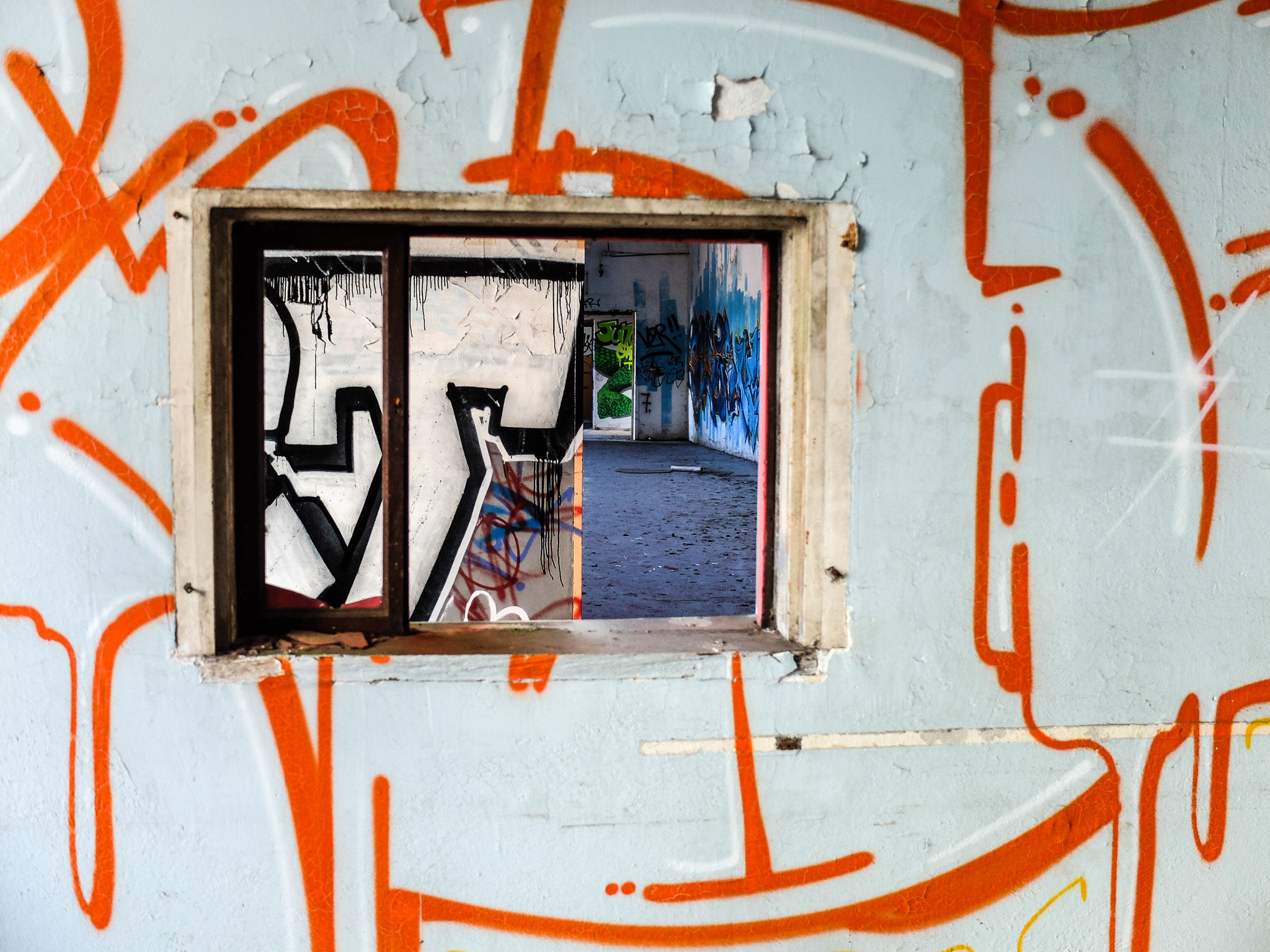 Ouverture rectangulaire entourée de graffitis orange et noirs sur un mur clair
