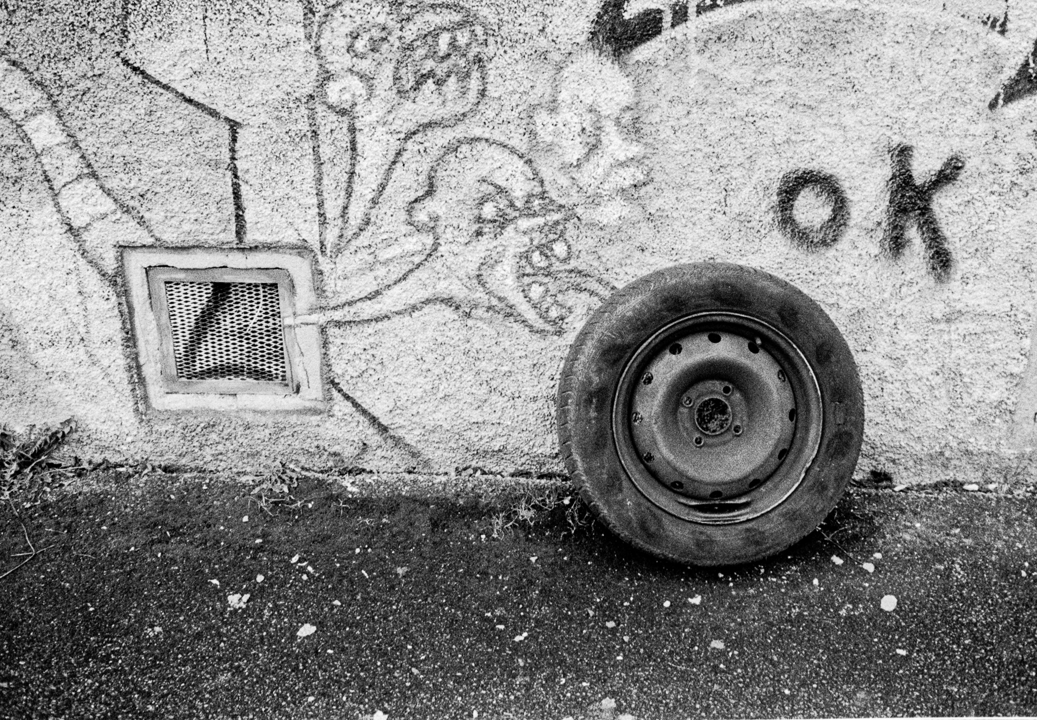 Roue appuyée contre un mur couvert de traces et de graffitis, photographiée en noir et blanc
