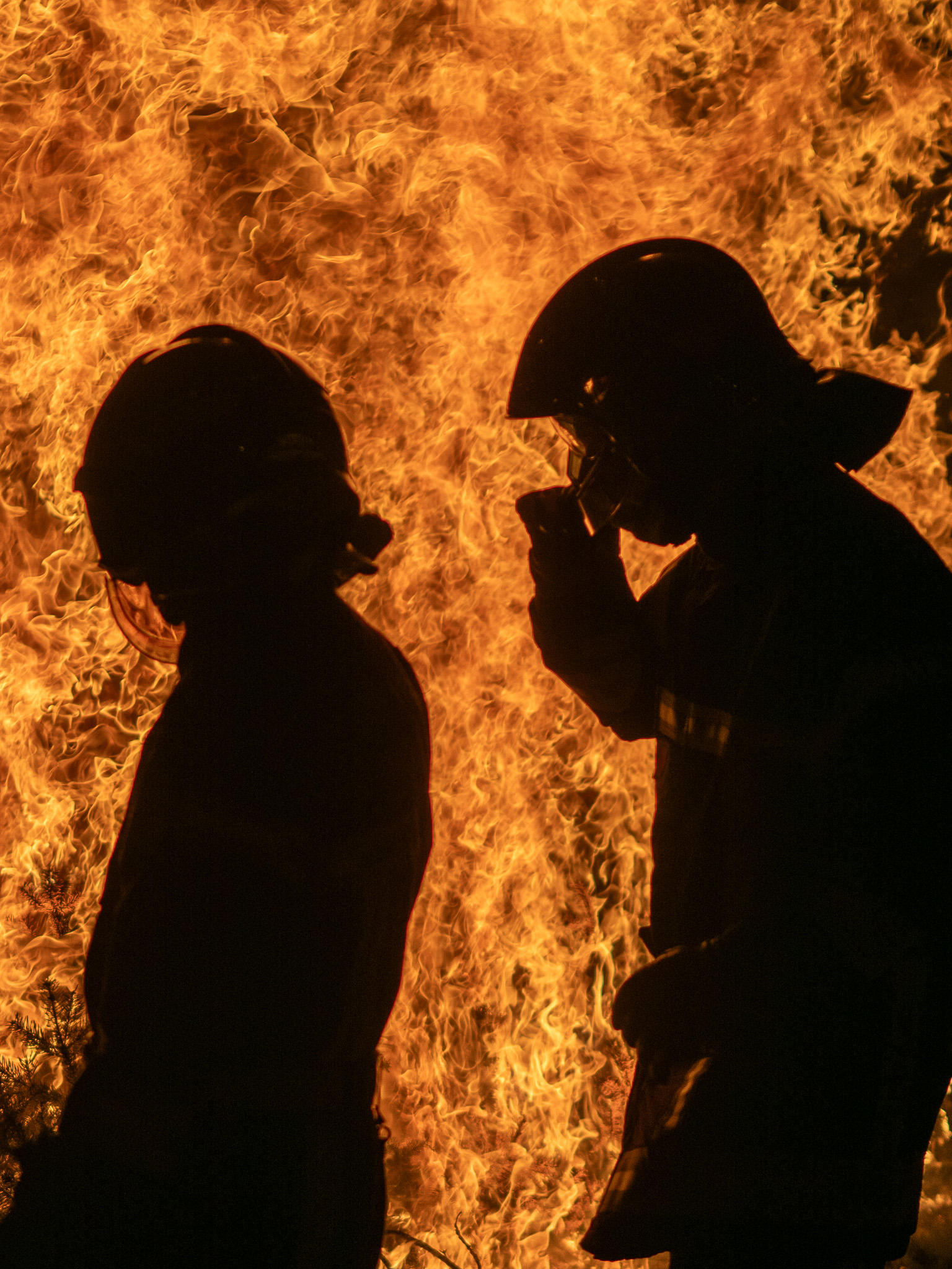 Deux sapeurs-pompiers en silhouette devant de hautes flammes lors d’un exercice nocturne