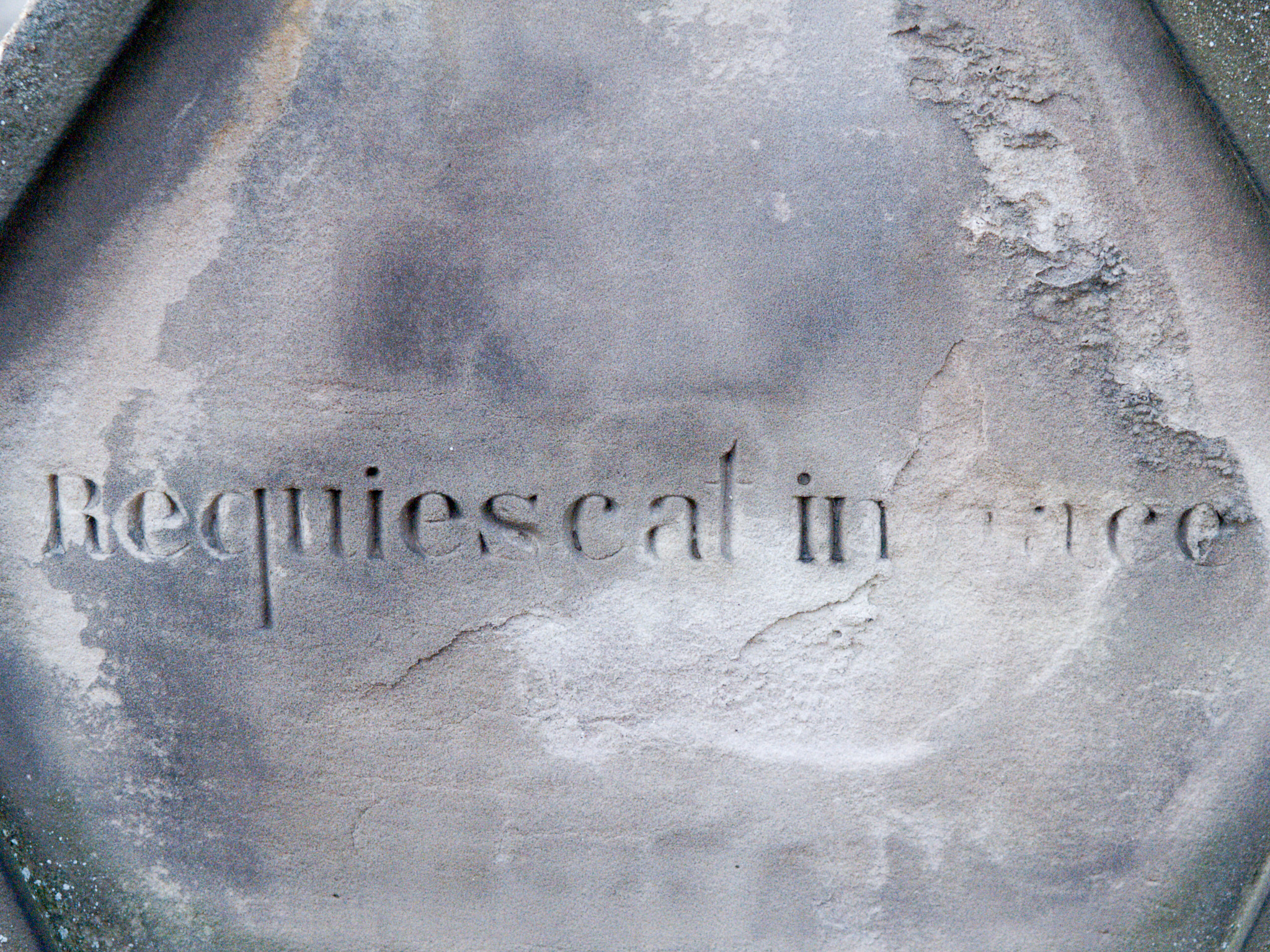 Inscription ancienne partiellement effacée gravée dans une surface de pierre sombre