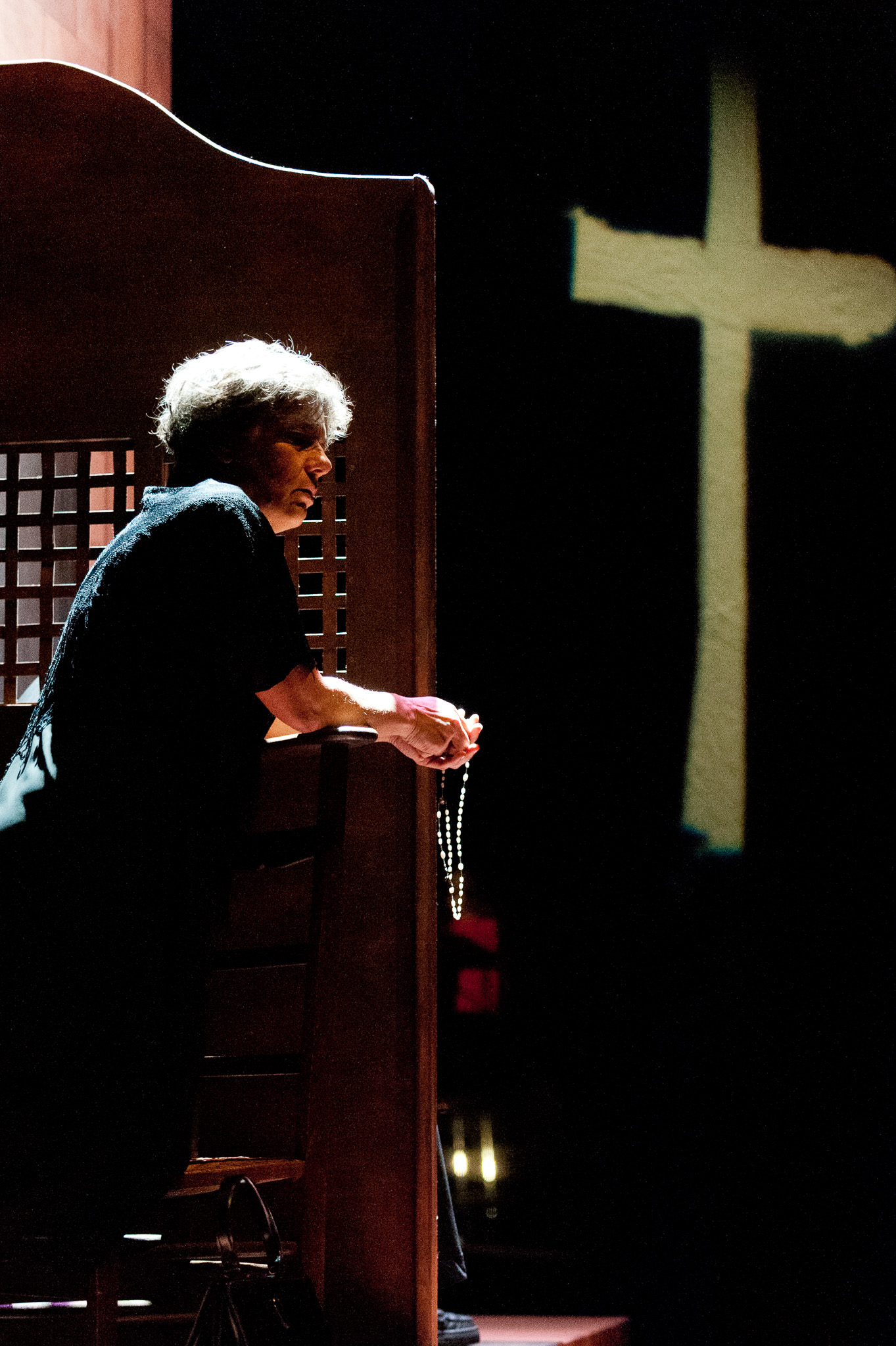 Comédienne de profil devant une grande croix projetée par la lumière sur le décor