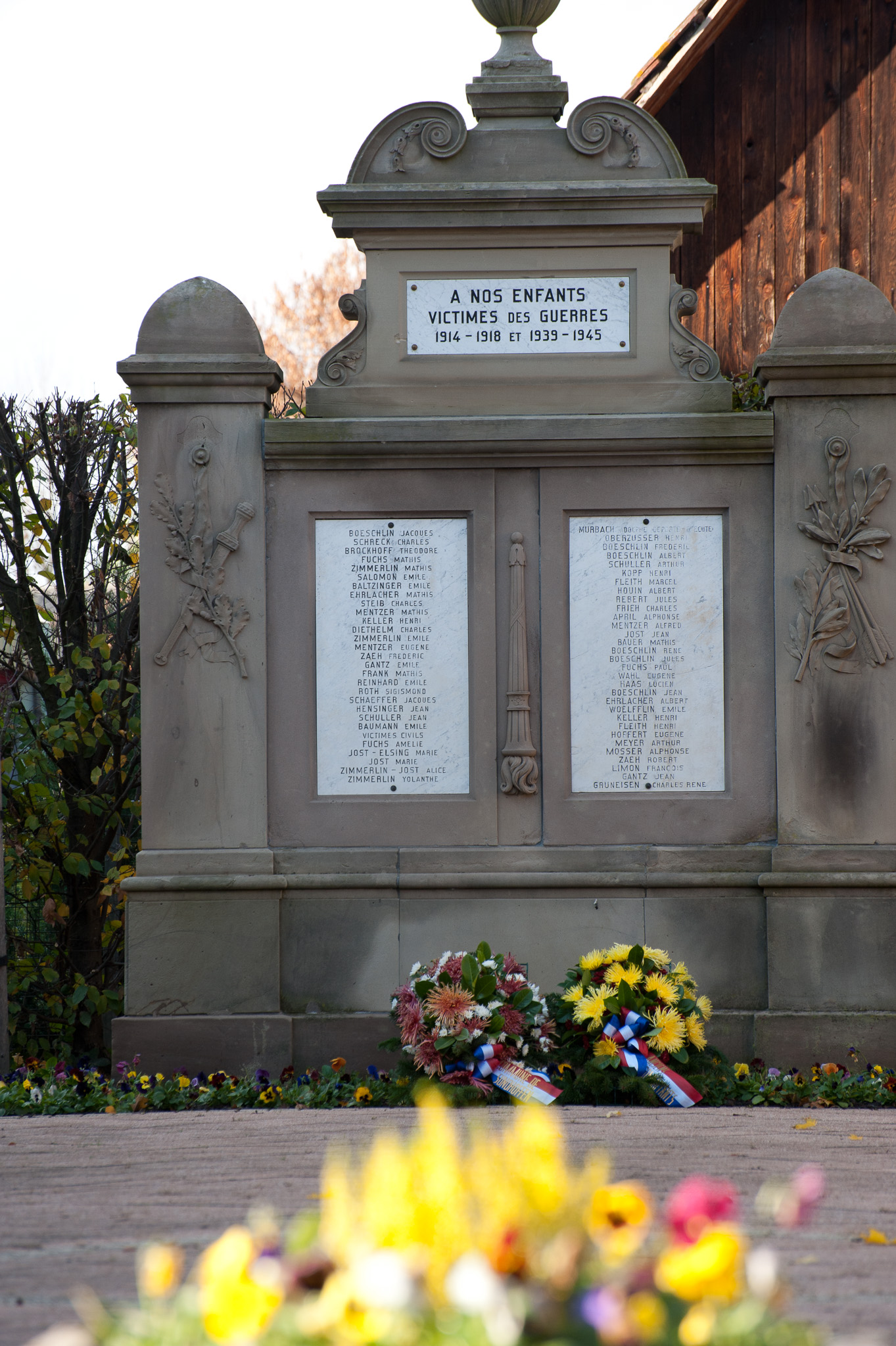 Monument aux morts de Sundhoffen portant les noms des victimes avec des fleurs déposées au premier plan
