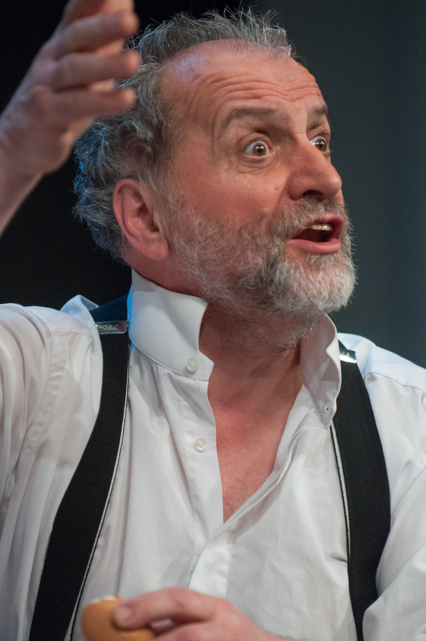 Comédien en chemise blanche et bretelles saisi dans un geste expressif pendant une représentation