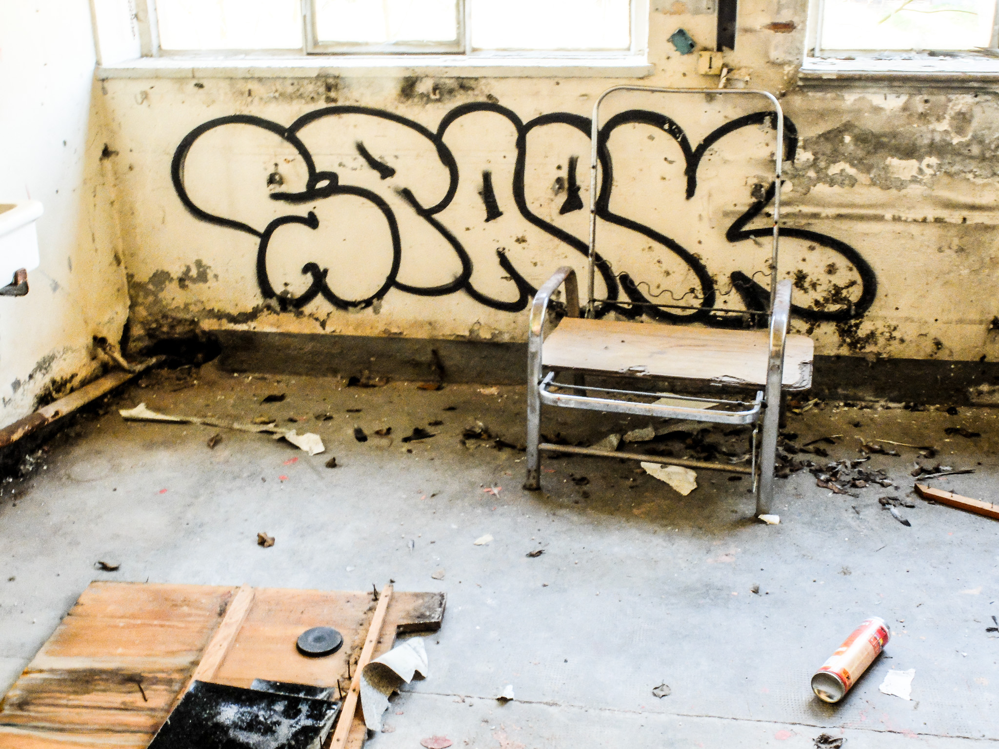 Graffiti noir, chaise métallique et débris dans une pièce abandonnée