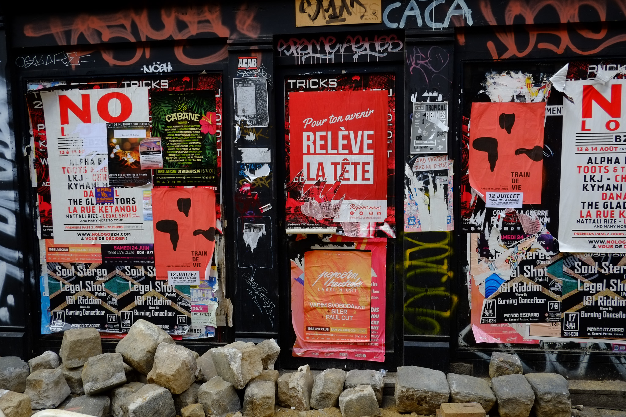 Façade urbaine couverte d’affiches rouges et noires, de slogans, d’autocollants et de graffitis