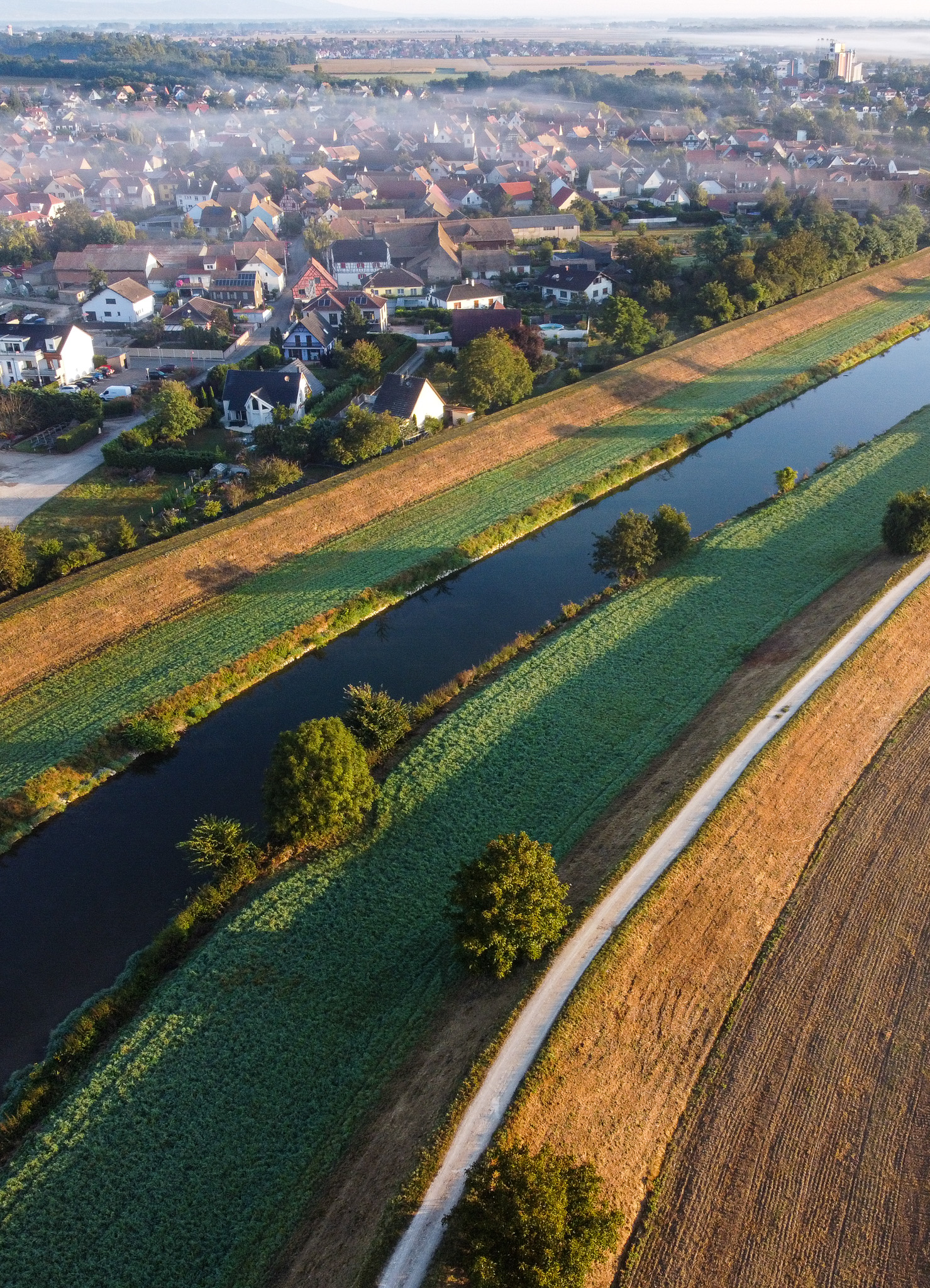 Vue aérienne du village de Sundhoffen au petit matin, bordé par l’Ill et les terres agricoles