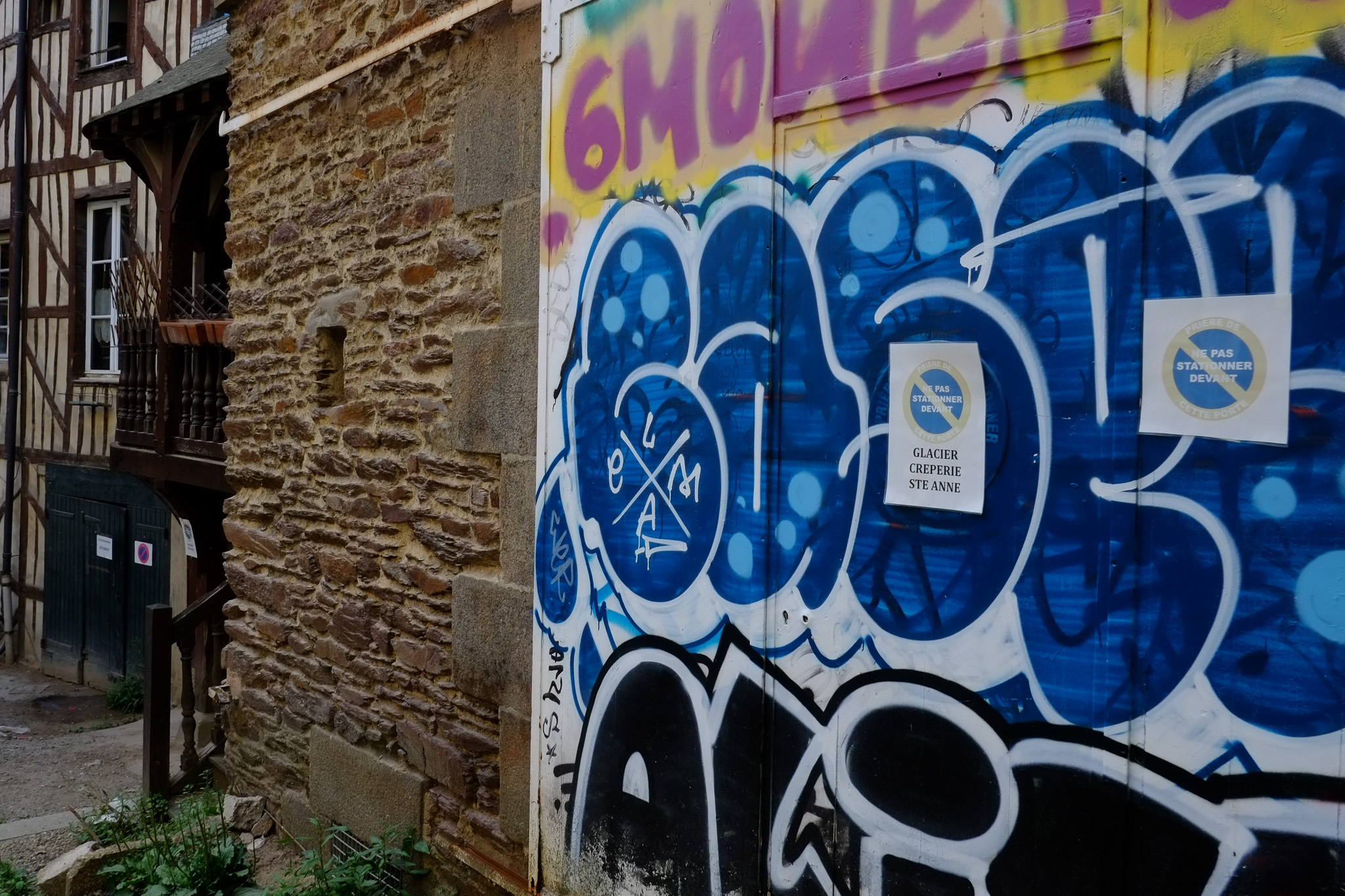 Graffiti bleu et noir peint sur un mur de pierre dans une ruelle ancienne