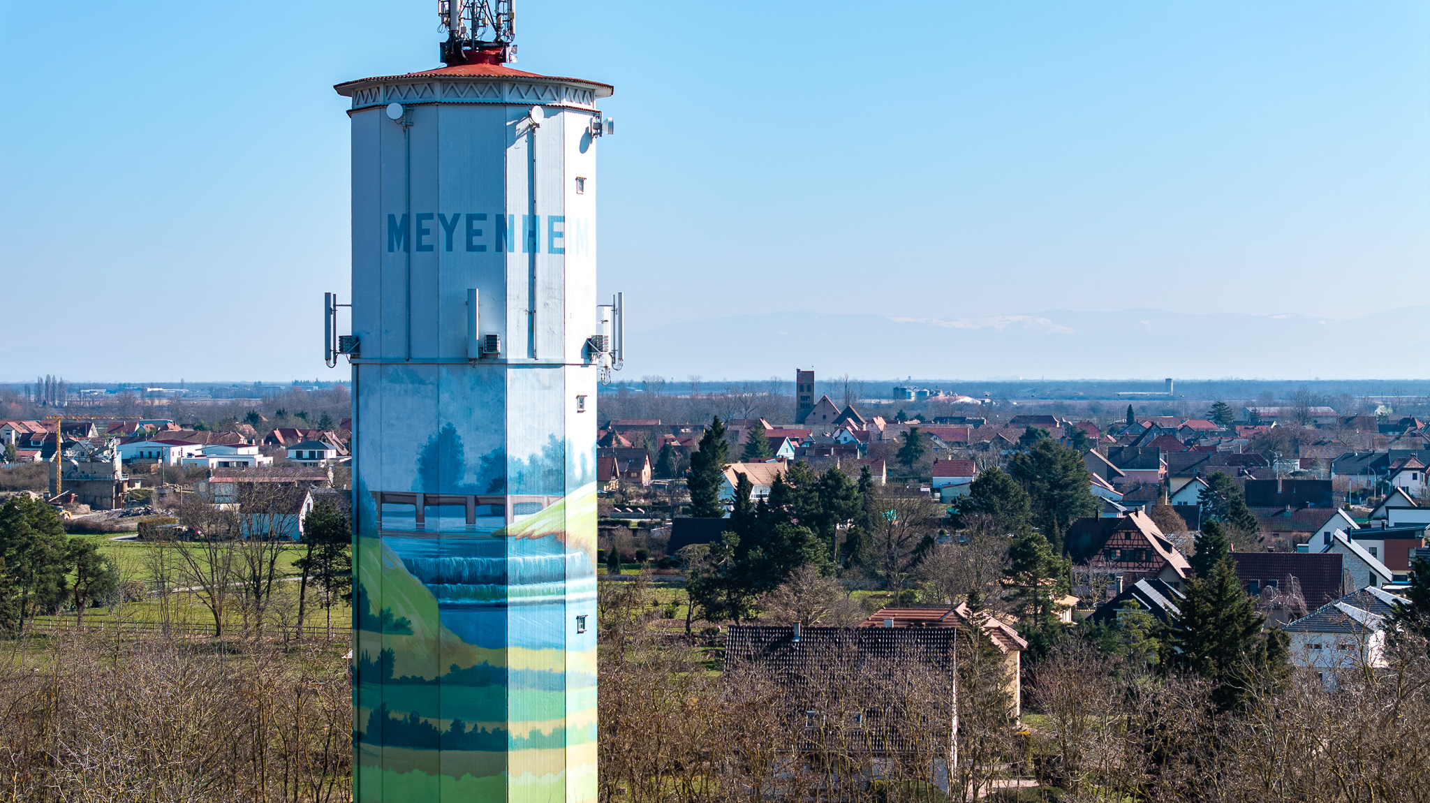 Vue aérienne du village de Meyenheim dominé par son château d’eau, au milieu de la plaine agricole